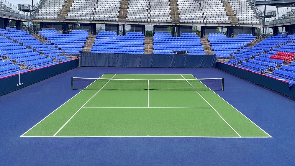 Why are synthetic court materials widely used in tennis court construction?